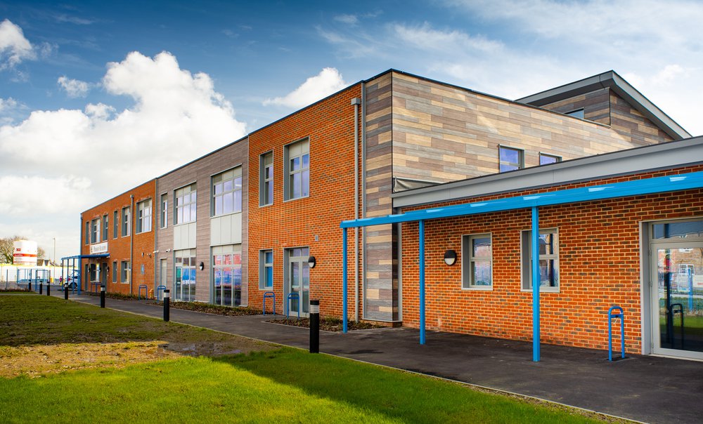 Front view of Hailsham School showing the orange brickwork and grey, blue and cream cladding to the right hand side