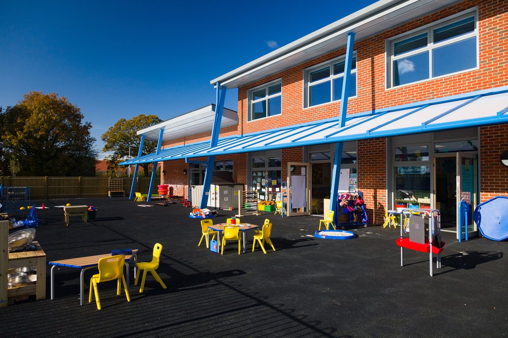 View of the playground area in front of the Hailsham School building, which features wooden tables and yellow seating