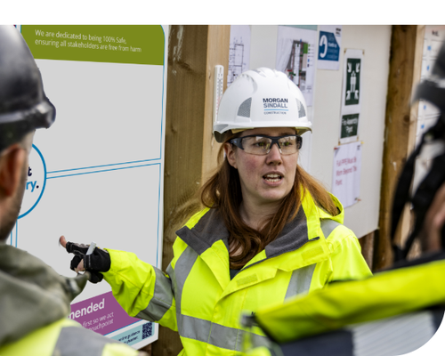 Female in personal protective wear on a construction site pointing to a whiteboard