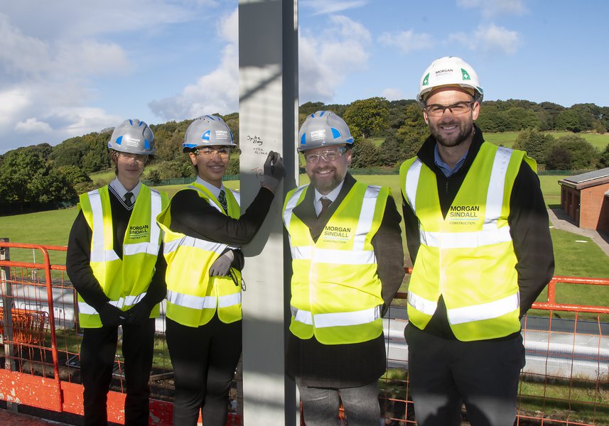 Four people at the steel signing event, with one person signing their name on the steel