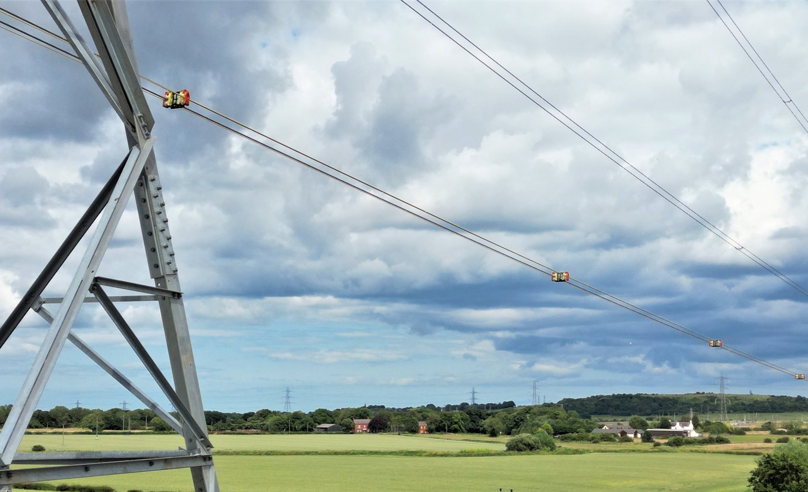A landscape image of the CatchBlock roller system in use on a power line, suspended from a tower.