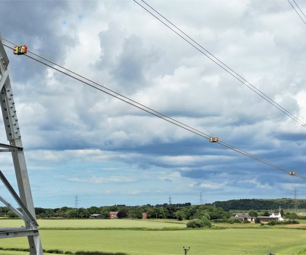 A landscape image of the CatchBlock roller system in use on a power line, suspended from a tower.