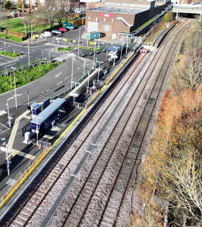 An aerial view of a train station with empty platforms, multiple train tracks, and a large parking lot with a few cars parked.