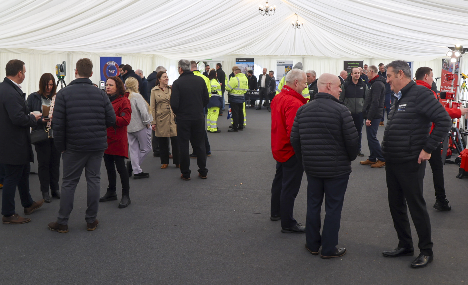 A photograph taken inside a marquee as part of the Green Plant Day event. Several people are stood in small groups, with items of plant and company banners can be seen in the background.