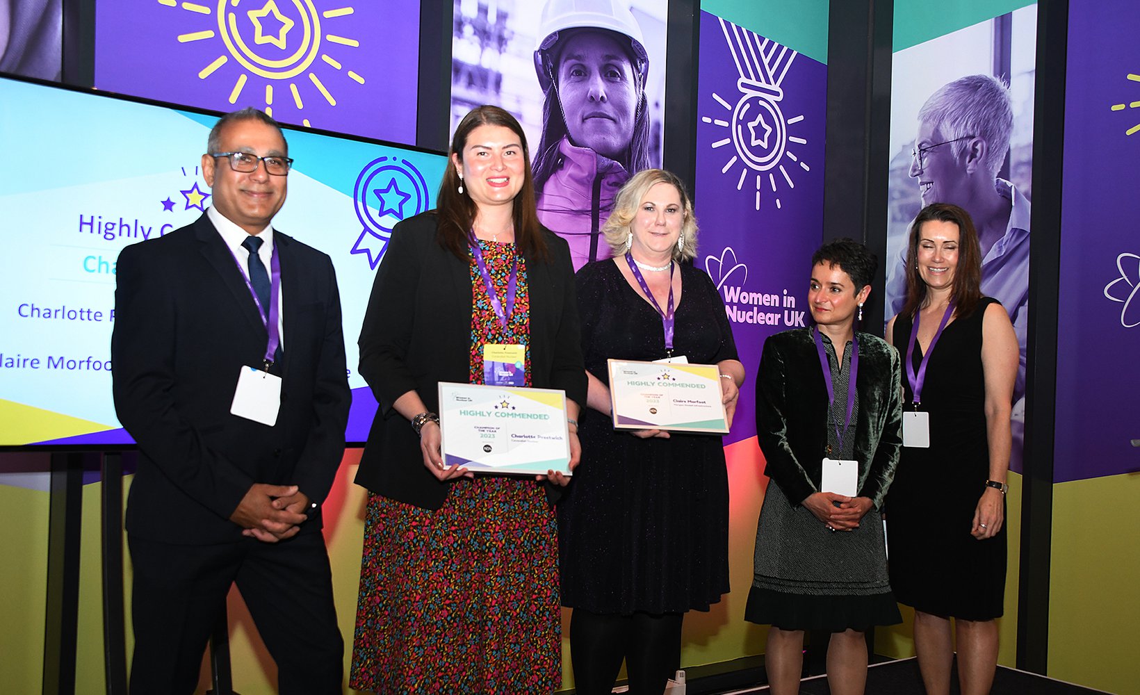 A group of five award winning colleagues from various companies stand on stage at the Women In Nuclear awards. Among them stands Morgan Sindall Infrastructure SHEQ manager Claire Morfoot, third from left