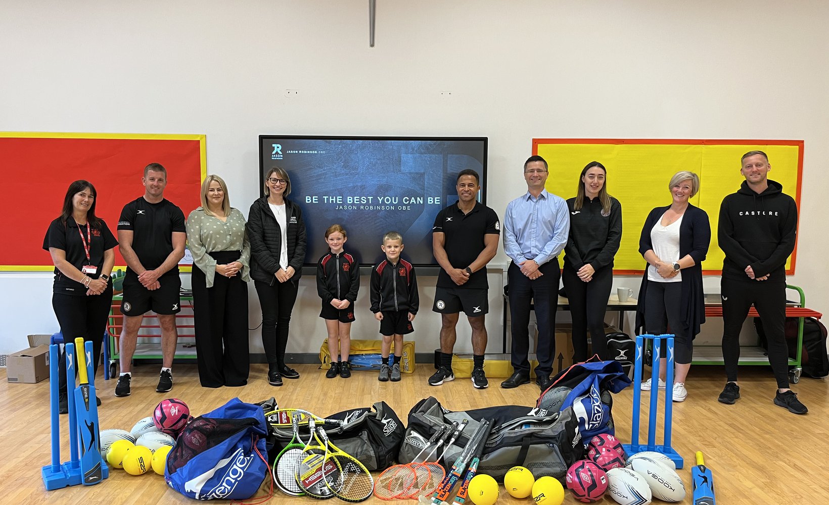 A photograph depicting Morgan Sindall colleagues, school staff members and pupils, and former Rugby player Jason Robinson OBE stood with sports equipment in a school hall