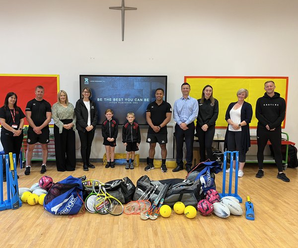 A photograph depicting Morgan Sindall colleagues, school staff members and pupils, and former Rugby player Jason Robinson OBE stood with sports equipment in a school hall
