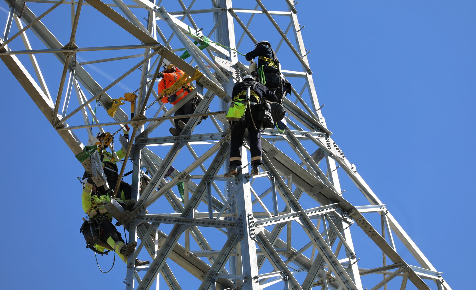Team members wearing Personal Protective Equipment (PPE) are pictured working on an electricity tower