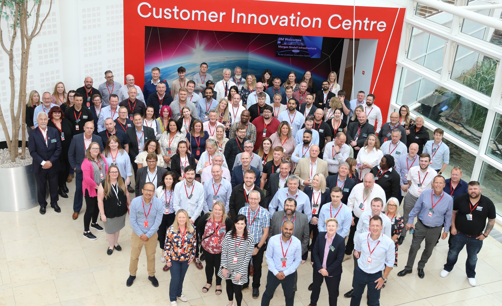A large group of Morgan Sindall Infrastructure colleagues stand assembled in a group as part of a company event. Photographed from above, they smile at the camera