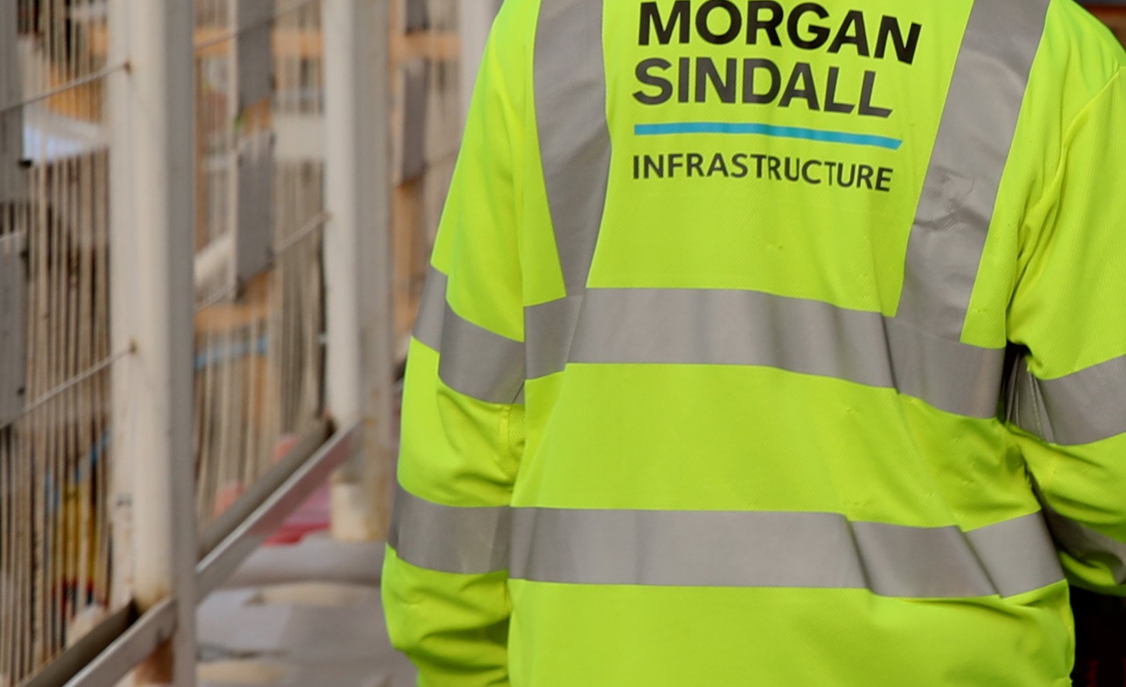 Two Morgan Sindall Infrastructure colleagues are pictured wearing Personal Protective Equipment, walking away from the camera
