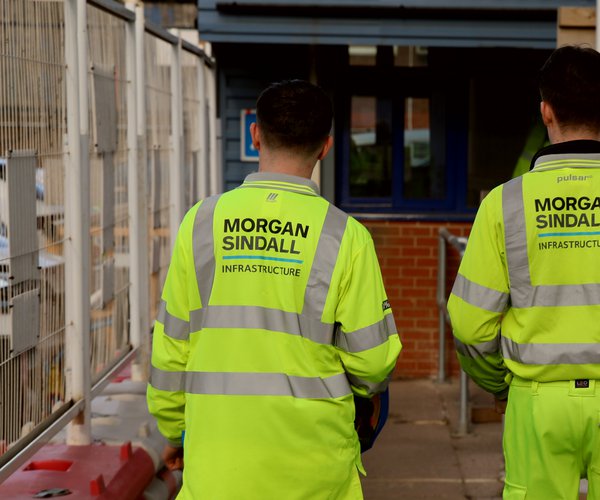 Two Morgan Sindall Infrastructure colleagues are pictured wearing Personal Protective Equipment, walking away from the camera