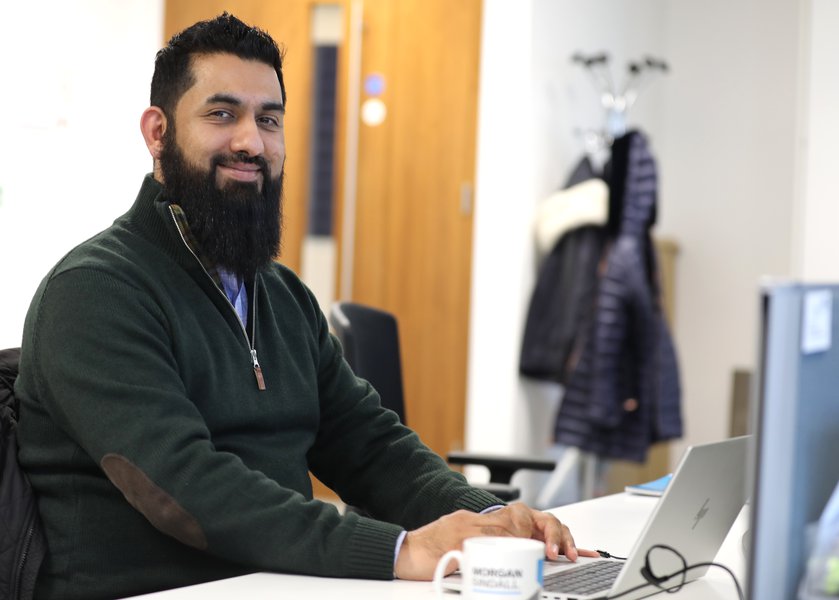 A photograph of Morgan Sindall Infrastructure colleague Zak Akhtar, sat at a desk, looking at the camera and smiling