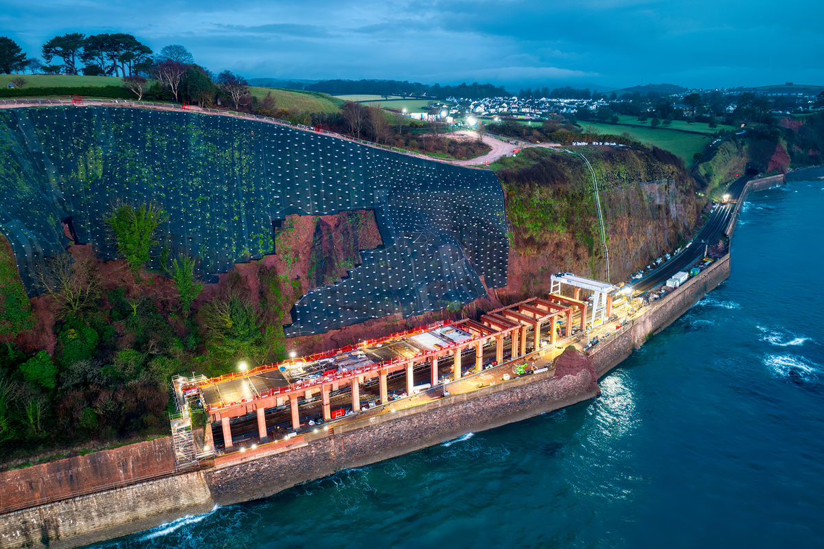 An aerial photograph of our Parson's Tunnel project, showing railway works and cliff stabilisation works, at dusk, lit up facing the sea